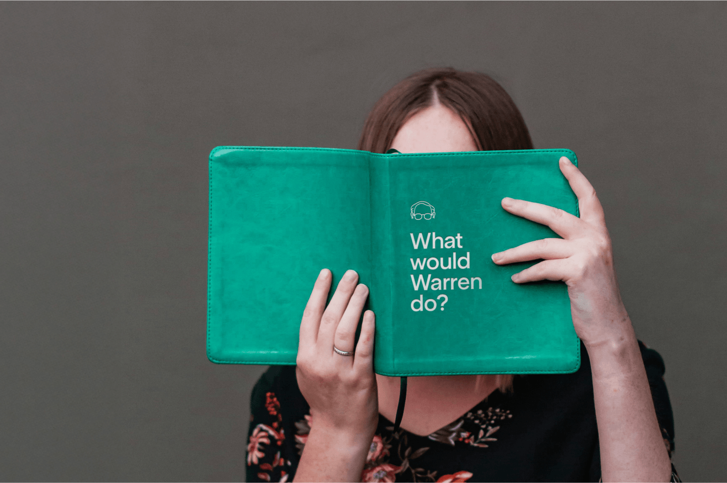 A woman reading a green book with the title What would Warren do?